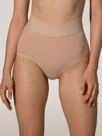 A close-up of a model wearing high-waisted, seamless underwear in a light nude beige color, shown from the waist to the upper thighs against a neutral studio background.