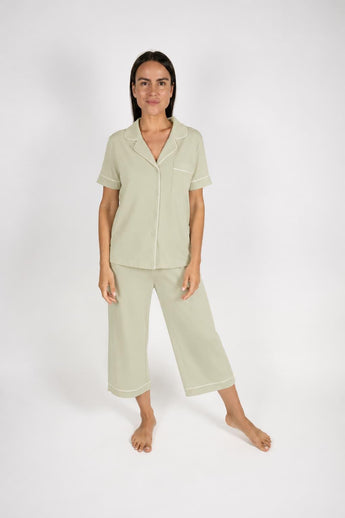 Sage green short-sleeve pajama top with notch collar, chest pocket, and white piping, paired with matching cropped wide-leg pajama pants,