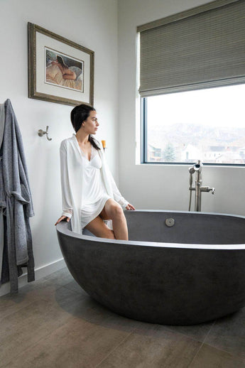Woman sitting in a modern freestanding bathtub in a bathroom wearing Aspen Dream's Nora Short Robe in Ivory