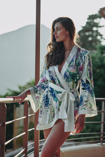 model wearing the Clea short robe by Marjolaine with a wrap front and self-tie belt in white with floral design