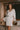 Model wearing the Marjolaine Tess Short Silk Robe in ivory featuring smooth silk satin, floral lace cuffs, a wrap-front design, long sleeves, and a self-tie waist belt.