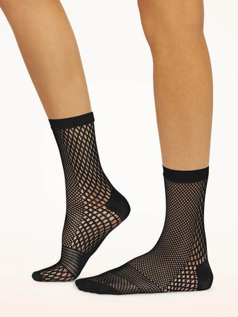 Model wearing Wolford Net Socks in black showing grid net pattern and ankle length