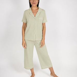 Sage green short-sleeve pajama top with notch collar, chest pocket, and white piping, paired with matching cropped wide-leg pajama pants,