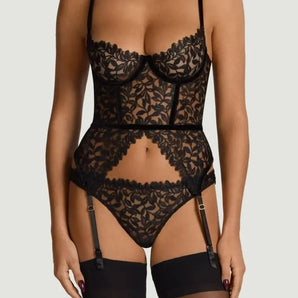 Black botanical embroidered basque with underwired balconette cups, velvet waistband, and suspender straps, worn with a matching thong