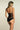 Back view of black bodysuit with sheer mesh back, adjustable straps with gold tone hardware, and V shaped waistband