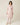 Model wearing blush pink Kenza Knitted Robe by Pluto with shawl collar and pom-pom trim .