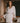 Model wearing the Marjolaine Tess Short Silk Robe in ivory featuring smooth silk satin, floral lace cuffs, a wrap-front design, long sleeves, and a self-tie waist belt.