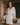 Model wearing the Marjolaine Tess Short Silk Robe in ivory featuring smooth silk satin, floral lace cuffs, a wrap-front design, long sleeves, and a self-tie waist belt.