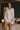 Model wearing the Marjolaine Tess Short Silk Robe in ivory featuring smooth silk satin, floral lace cuffs, a wrap-front design, long sleeves, and a self-tie waist belt.
