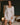 A woman models a white satin lingerie set consisting of a lace-trimmed slip and a matching open-front robe in a dimly lit bedroom setting.