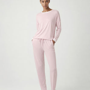 Woman wearing the Pluto Aadia Abelone Pajama Set in soft pink featuring a long sleeve crew neck top and tapered cotton modal pajama pants.