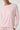 A close-up of a model wearing a light pink long-sleeve crewneck top with contrasting white trim at the collar and cuffs, paired with matching pink bottoms.