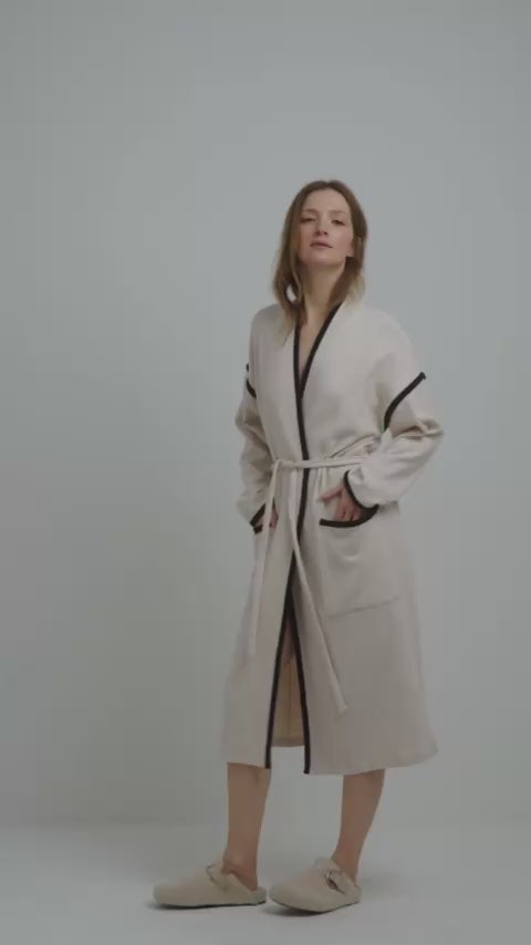 Model wearing the pluto priska robe in beige with black trim, shawl collar, and tie waist