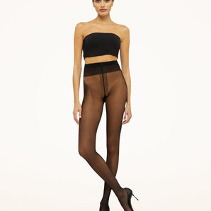 Model wearing Wolford Individual 10 Tights in black showing sheer finish and soft waistband.